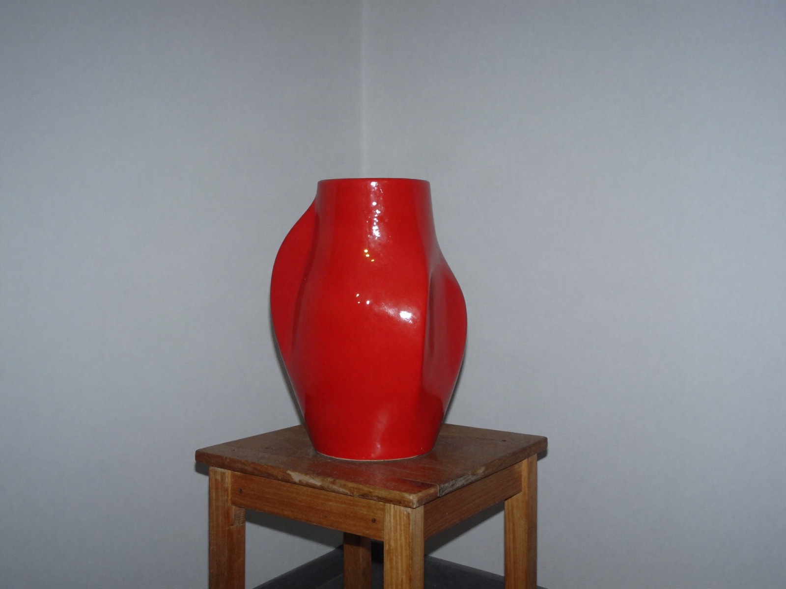 Pieza escultórica roja fotografiada con flash frontal en un rincón oscuro, estética digicam de los 2000