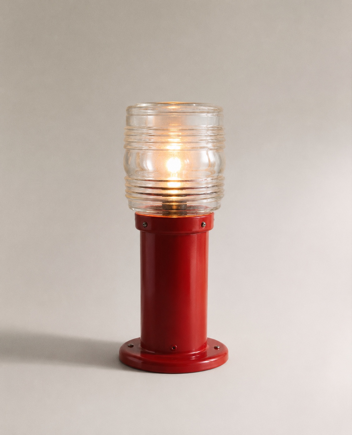 Luminaria Faro, lámpara roja esmaltada encendida sobre fondo neutro