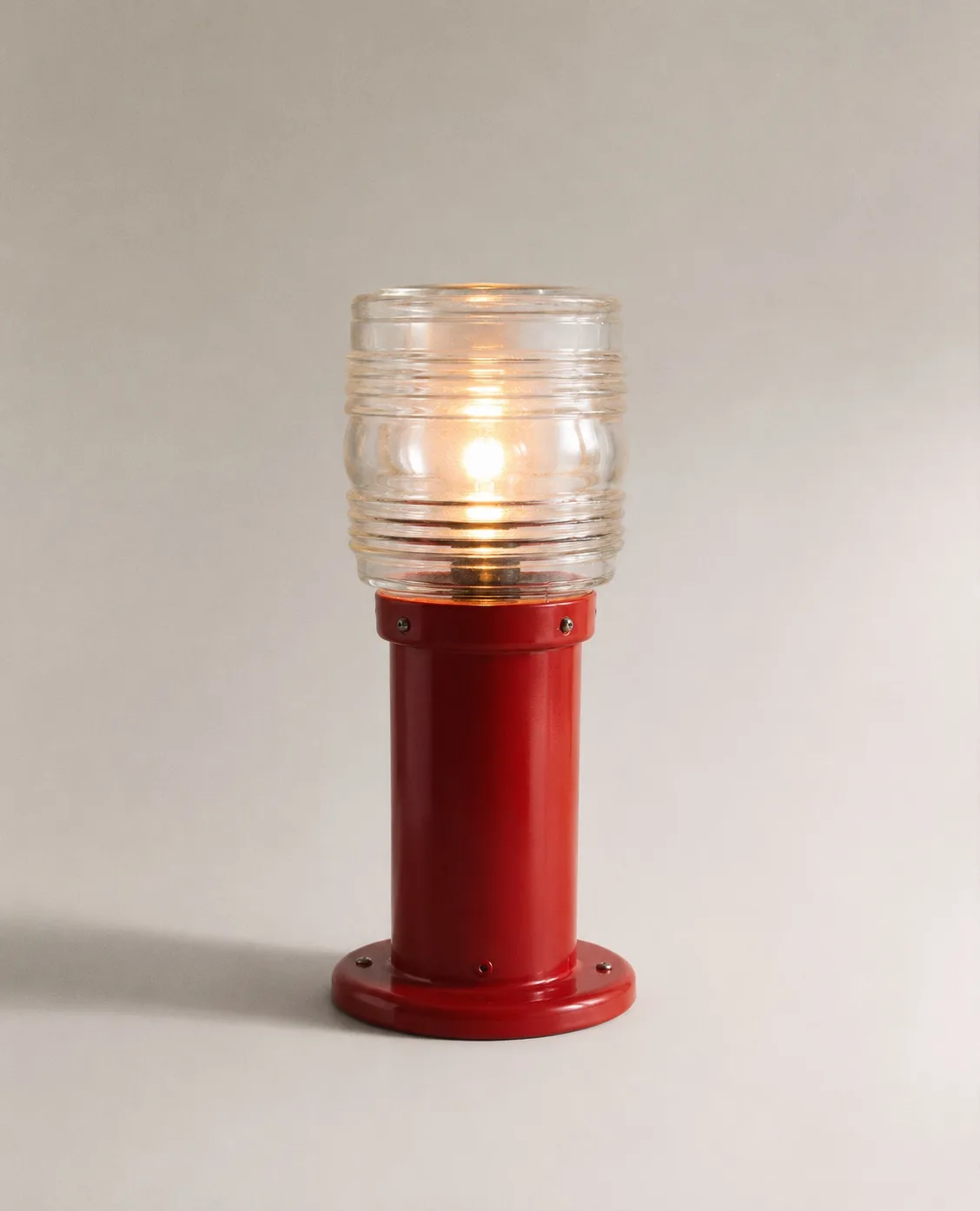 Luminaria Faro, lámpara roja esmaltada encendida sobre fondo neutro